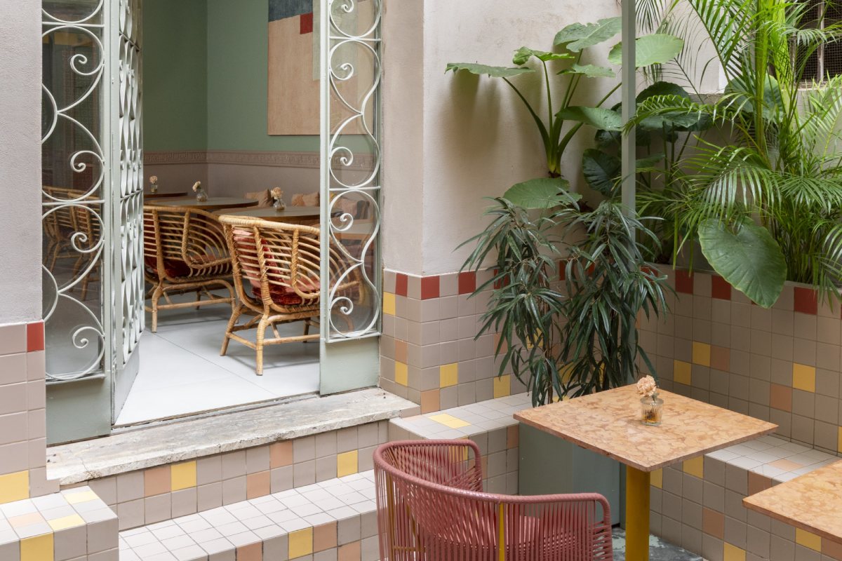 Internal courtyard with outdoor tables, wicker chairs, and pink armchairs, surrounded by tropical plants and colorful tiled walls - Hotel Milani, BZAR hotels in Rome