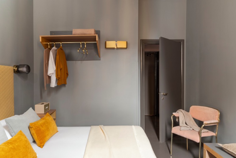 Connecting Family room detail showing grey entrance door, open wardrobe rack and pink armchair - Hotel Milani, BZAR hotels in Rome
