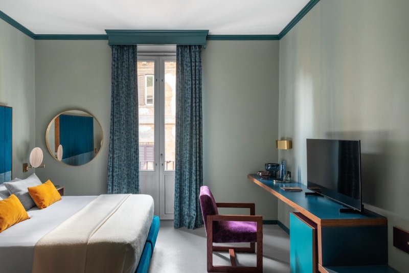 Spacious Superior room featuring a blue designer desk, purple velvet armchair, and large bright window with patterned curtains - Hotel Milani, BZAR hotels in Rome