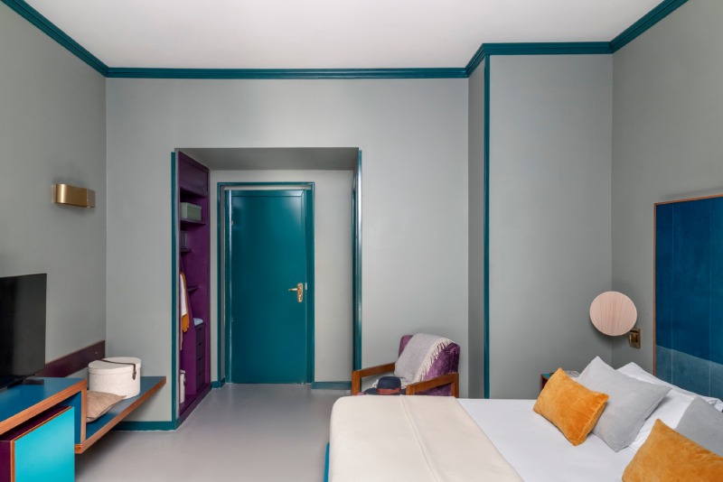 Superior room interior with blue headboard, ochre pillows and contrasting purple built-in wardrobe detail - Hotel Milani, BZAR hotels in Rome
