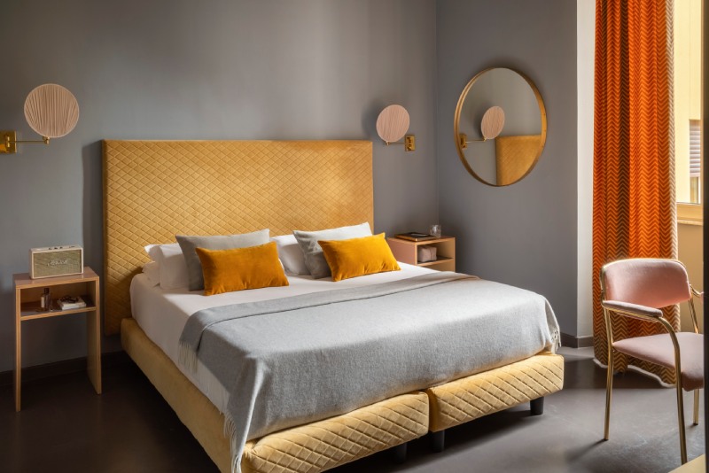 Design triple room with double bed, mustard yellow headboard, grey walls, and pink velvet chair - Hotel Milani, BZAR hotels in Rome