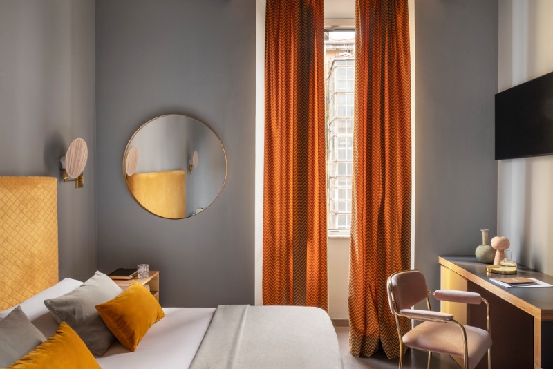 Triple room detail featuring window view with orange curtains, golden circular mirror, and modern desk - Hotel Milani, BZAR hotels in Rome
