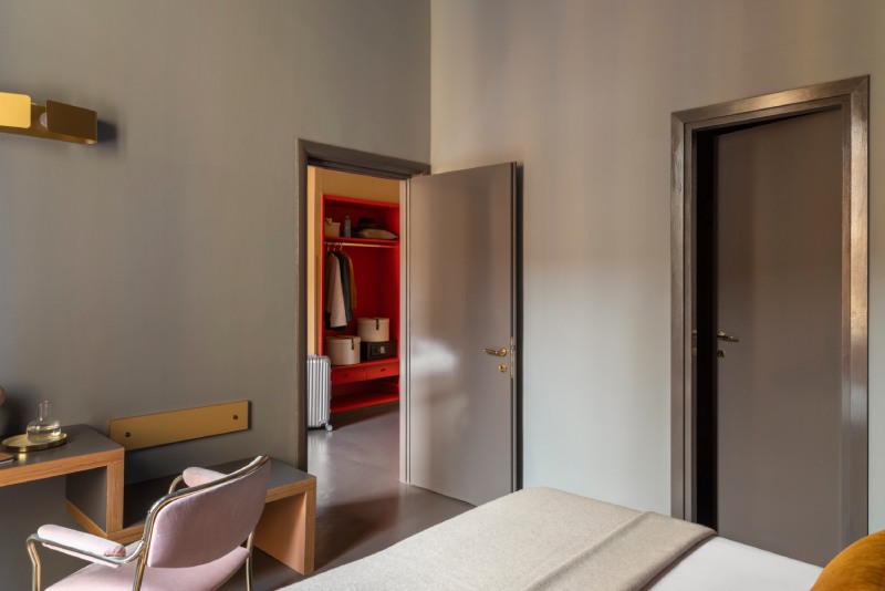 Separate living area of a triple room with ochre walls, round rattan table, extra single bed, and silver suitcase - Hotel Milani, BZAR hotels in Rome